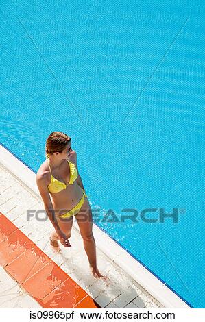 Stock Image - Young woman walking by poolside. Fotosearch