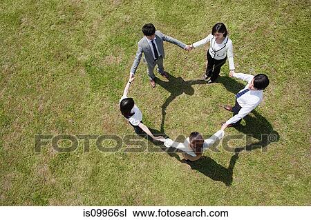 Stock Image - Businesspeople in a circle in field, high angle. Fotosearch