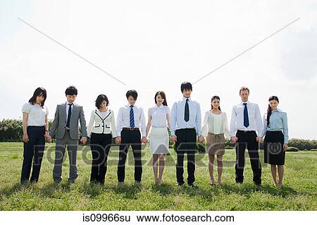 Stock Photograph - Businesspeople in a row in field, holding hands. Fotosearch