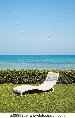 Stock Image - Empty white sun lounger on grass. Fotosearch