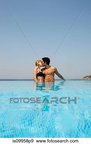 Stock Photo - Young couple kissing in infinity pool. Fotosearch
