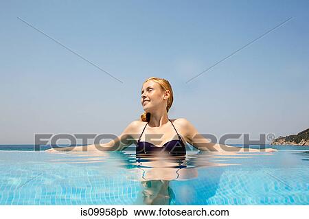 Stock Image - Young woman in infinity pool, looking away. Fotosearch