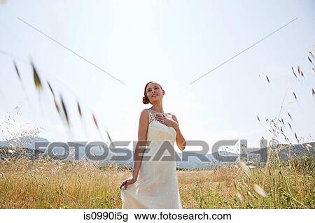 Stock Image - Bride wearing wedding dress alone in field. Fotosearch