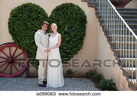 Stock Image - Newlyweds by heart shaped bush. Fotosearch