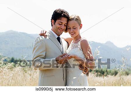 Newlyweds in field looking at wedding ring View Large Photo Image Stock Image - Newlyweds in field looking at wedding ring. Fotosearch