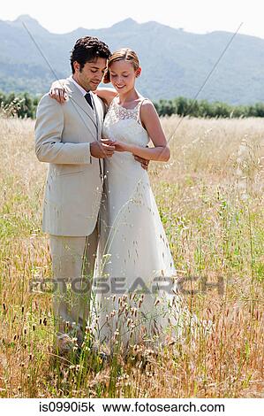 Newlyweds in field looking at wedding ring View Large Photo Image Stock Image - Newlyweds in field looking at wedding ring. Fotosearch
