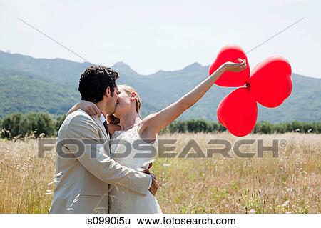 Newlyweds kissing in field with red heart shape balloons View Large Photo Image Stock Photograph - Newlyweds kissing in field with red heart shape balloons. Fotosearch