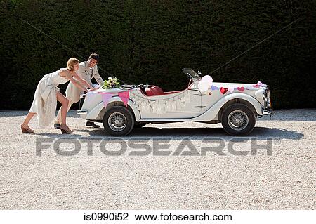 Stock Image - Newlyweds pushing broken down vintage car. Fotosearch