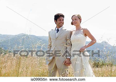 Newlyweds walking in field, holding hands View Large Photo Image Picture - Newlyweds walking in field, holding hands. Fotosearch