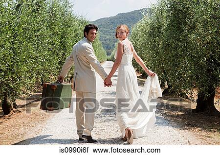 Stock Image - Newlyweds walking on country road with suitcase. Fotosearch