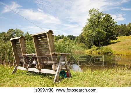A double wooden chair positioned by a lake View Large Photo Image Stock Photo - A double wooden chair positioned by a lake. Fotosearch