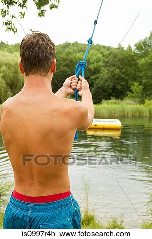 Stock Image - Teenage boy about to swing across a lake. Fotosearch