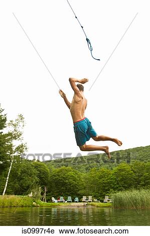 Stock Image - Teenage boy swinging off a rope into a lake. Fotosearch
