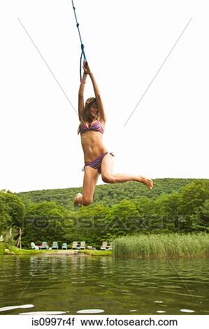 Stock Image - Teenage girl swinging on a rope over a lake. Fotosearch