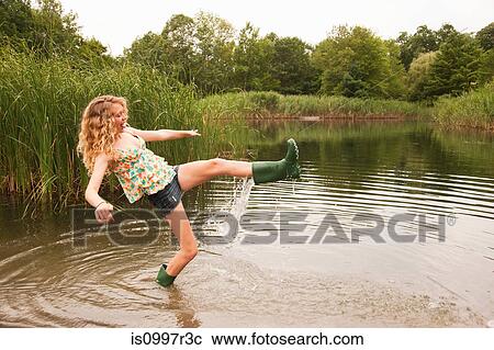 Stock Image - Teenage girl wading into the middle of a lake with over-flowing wellies. Fotosearch