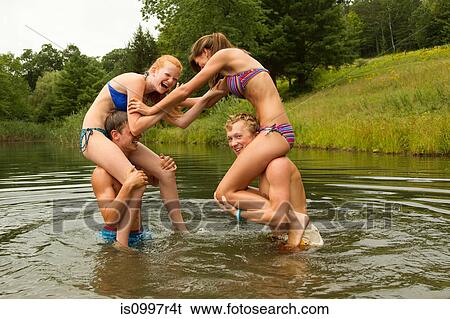 Stock Photograph - Teenage girls sitting on boys' shoulders in lake. Fotosearch