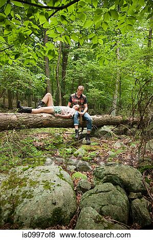 Couple relaxing together on log in forest View Large Photo Image Stock Photo - Couple relaxing together on log in forest. Fotosearch