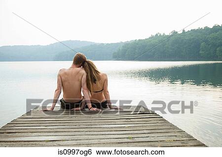 Couple sitting on pier looking over lake View Large Photo Image Stock Photograph - Couple sitting on pier looking over lake. Fotosearch