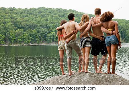 Friends standing together on rock at lakeside View Large Photo Image Stock Photo - Friends standing together on rock at lakeside. Fotosearch