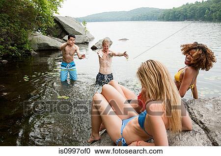Stock Image - Men splashing friends at lake. Fotosearch