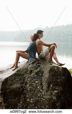 Stock Image - Young couple leaning on each other on rock. Fotosearch