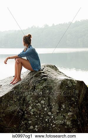 Young woman sitting on rock overlooking lake View Large Photo Image Stock Image - Young woman sitting on rock overlooking lake. Fotosearch
