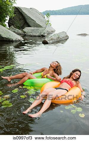 Stock Image - Young women floating on lake with inflatable rings. Fotosearch