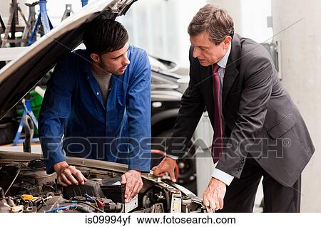 Stock Image - Businessman looking at car engine with mechanic. Fotosearch