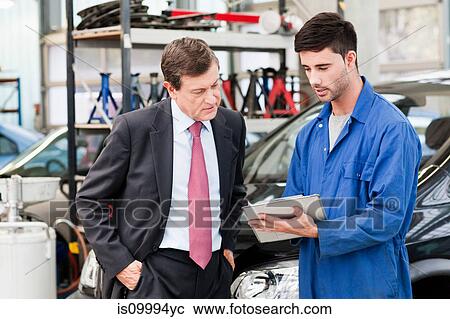 Stock Image - Businessman with car mechanics in repair garage. Fotosearch