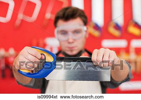 Carpenter holding saw in front of wood work tools View Large Photo Image Stock Photograph - Carpenter holding saw in front of wood work tools. Fotosearch