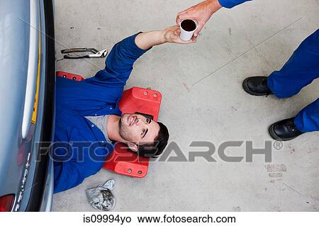 Mechanic passing coffee to colleague on floor View Large Photo Image Picture - Mechanic passing coffee to colleague on floor. Fotosearch