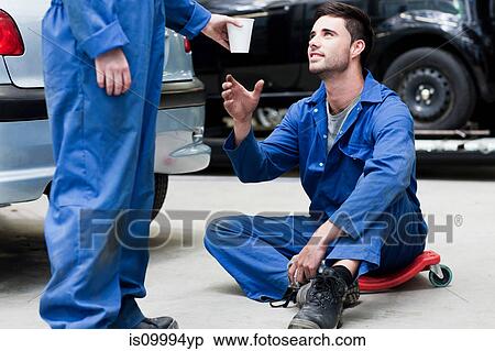 Mechanic passing coffee to colleague on floor View Large Photo Image Stock Photography - Mechanic passing coffee to colleague on floor. Fotosearch