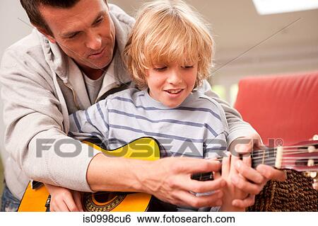 Father showing his son how to play a guitar View Large Photo Image Stock Photograph - Father showing his son how to play a guitar. Fotosearch