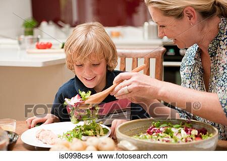 Picture - Mother serving salad to son at dining table. Fotosearch