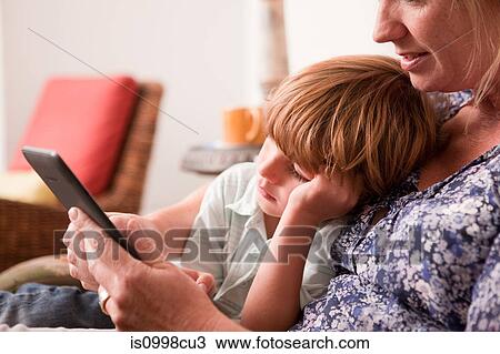 Stock Image - Son sitting next to mother while she uses a digital tablet. Fotosearch