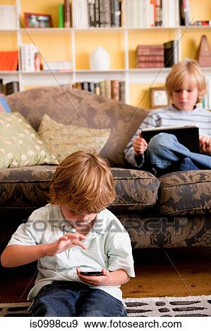 Two boys relaxing at home with a digital tablet and smart phone View Large Photo Image Stock Photo - Two boys relaxing at home with a digital tablet and smart phone. Fotosearch