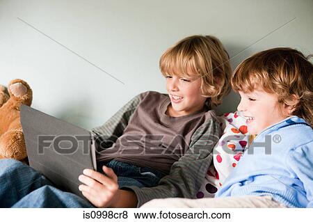 Two young boys on a bed, using a digital tablet View Large Photo Image Stock Photo - Two young boys on a bed, using a digital tablet. Fotosearch