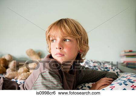Young boy lying on bed staring into distance View Large Photo Image Stock Photograph - Young boy lying on bed staring into distance. Fotosearch