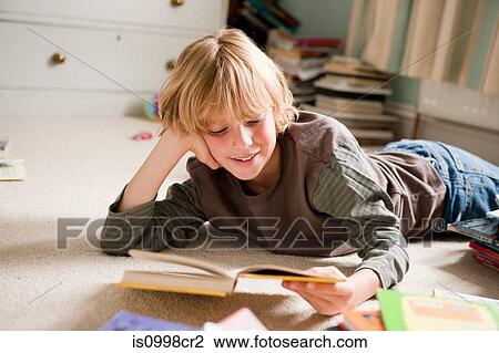 Young boy lying on his front, reading a book in his bedroom View Large Photo Image Stock Image - Young boy lying on his front, reading a book in his bedroom. Fotosearch
