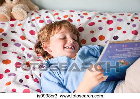 Stock Image - Young boy reading a book on his bed. Fotosearch