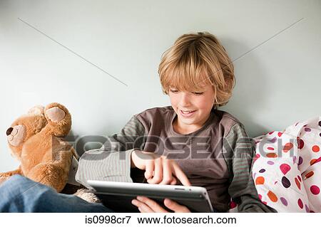 Young boy using a digital tablet while sitting on his bed View Large Photo Image Stock Photo - Young boy using a digital tablet while sitting on his bed. Fotosearch