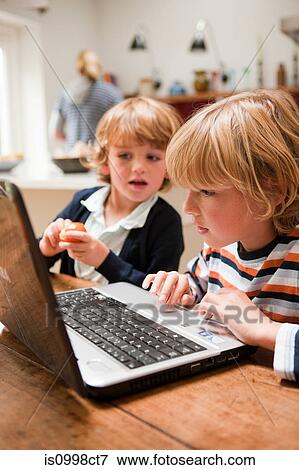 Young boy using laptop with his younger brother looking across at the monitor View Large Photo Image Stock Photo - Young boy using laptop with his younger brother looking across at the monitor. Fotosearch