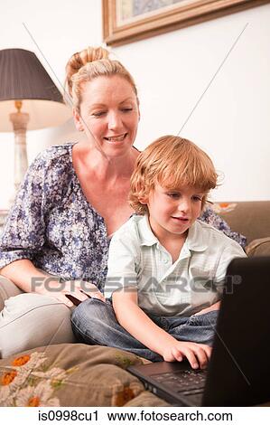 Young boy using laptop with mother looking on encouragingly View Large Photo Image Stock Image - Young boy using laptop with mother looking on encouragingly. Fotosearch