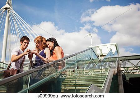 Three people looking at a mobile phone on Hungerford Bridge, London View Large Photo Image Stock Photograph - Three people looking at a mobile phone on Hungerford Bridge, London. Fotosearch