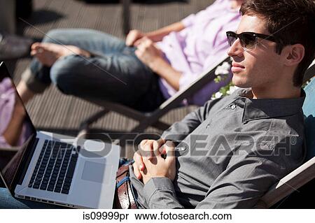 Stock Photography - Two men relaxing on deck chairs with a laptop. Fotosearch