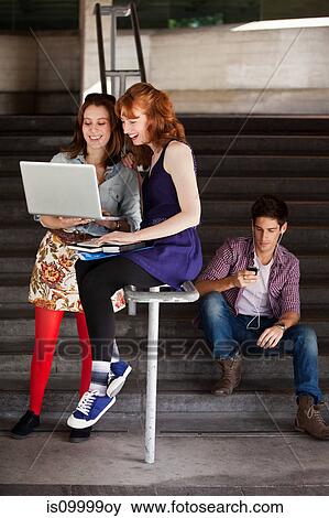 Two young woman looking at a laptop at the bottom of steps View Large Photo Image Stock Photo - Two young woman looking at a laptop at the bottom of steps. Fotosearch