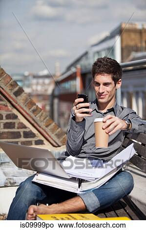 Picture - Young man sitting in a roof garden with laptop and mobile phone. Fotosearch