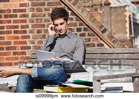 Picture - Young man sitting on a bench with a digital tablet and mobile phone. Fotosearch