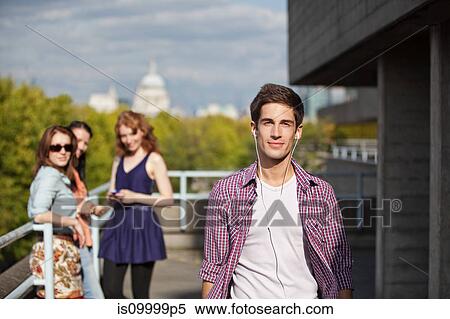 Young man walking along listening to earphones View Large Photo Image Stock Photography - Young man walking along listening to earphones. Fotosearch