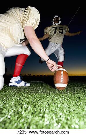 American football player attempting to kick field goal, teammate